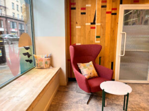 A photograph of the interior of the Nook in Glasgow, showing a cosy seating area with a window seat and a red armchair next to a small table.