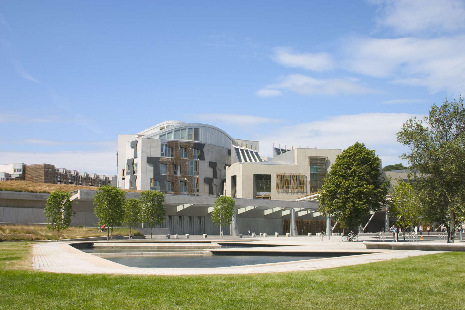 A photo of the exterior of the Scottish Parliament in Edinburgh, Scotland. Green grass in the foreground, blue sky above.