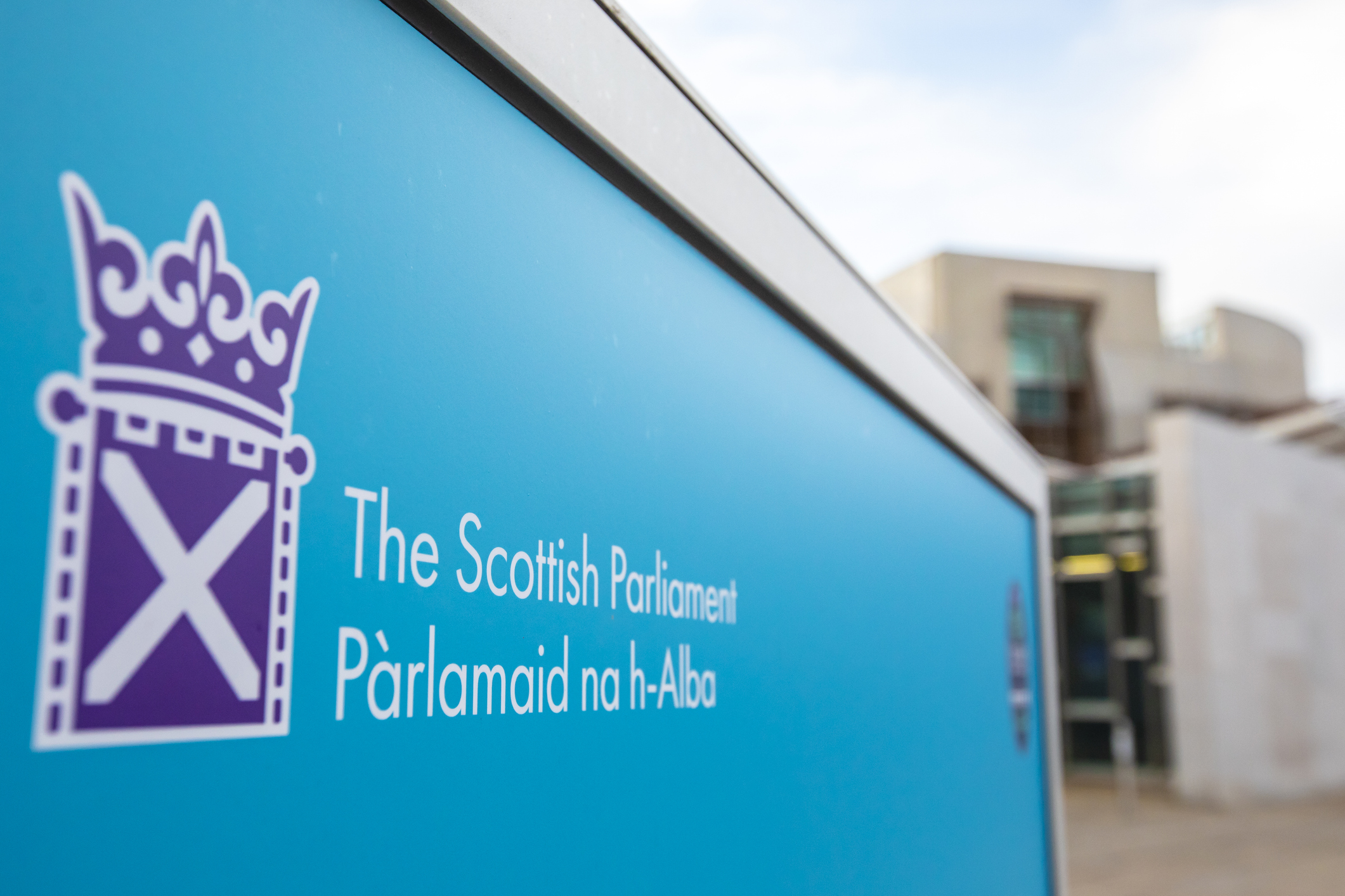 A sign in front of the Scottish Parliament building with 'Scottish Parliament' written in English and Gaelic